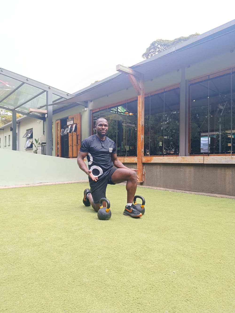 Tim kneeling on the grass with two kettlebells, smiling